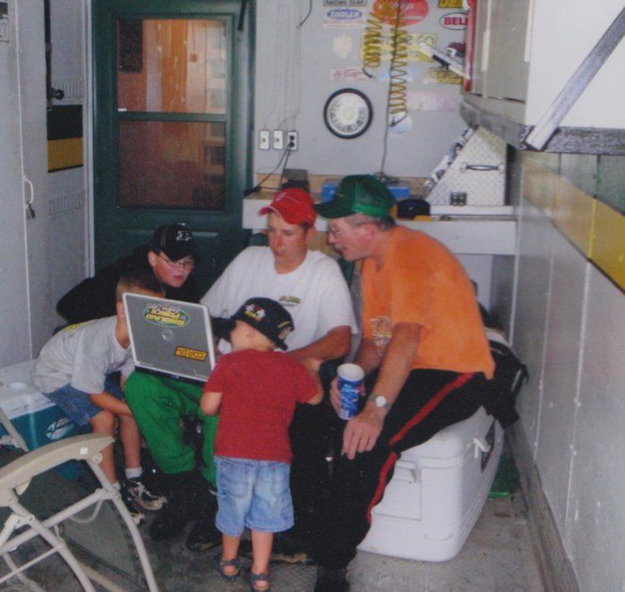 Men and children gathered inside a trailer, looking at a laptop.