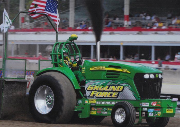 Green John Deere tractor in a tractor pull, pulling a weight sled, billowing black smoke.