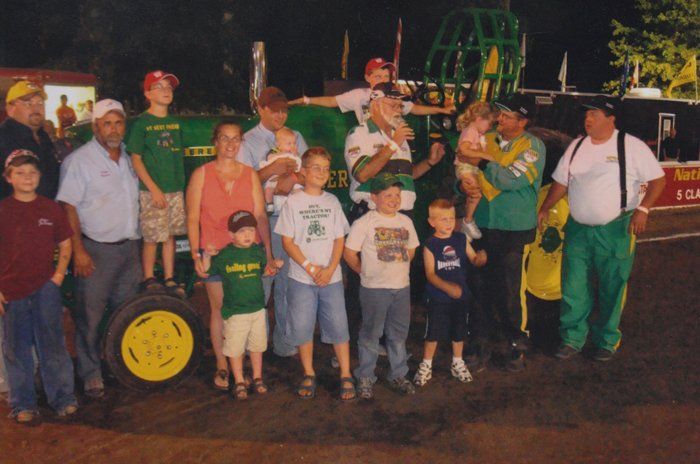 Group of people posing with a green and yellow tractor at night.