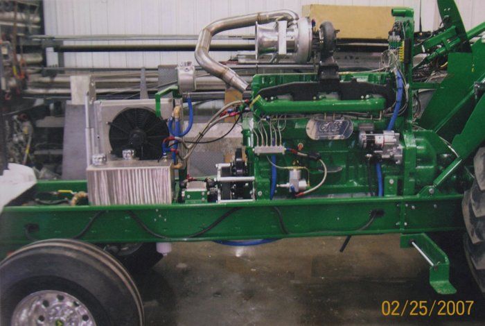 Green tractor engine components, silver turbo, various tubes and wires, in a shop setting.
