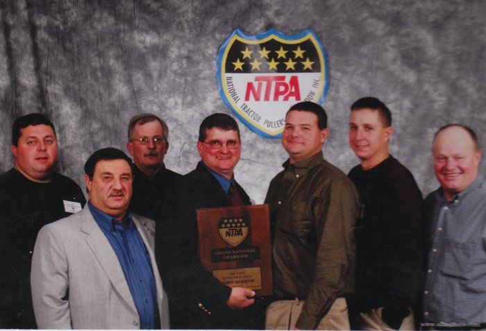 Group of men hold award in front of an NTPA logo backdrop. They are smiling, posing for a photo.