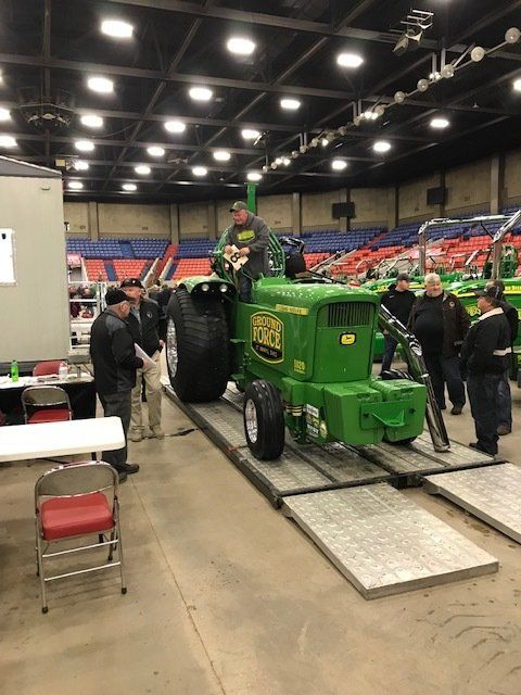 Green tractor on ramps, surrounded by people in a large indoor space.