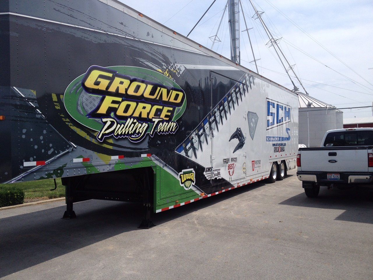 Ground Force Pulling Team semi-trailer with graphics, parked next to a pickup truck and grain silo.