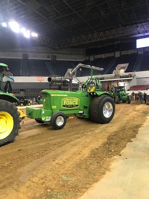 Green tractor pulling in an arena; dirt track. 