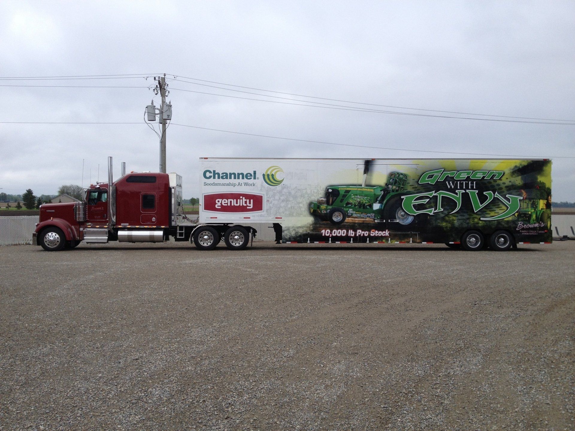 A maroon semi-truck pulling a trailer with a Channel branded design on a gravel surface.