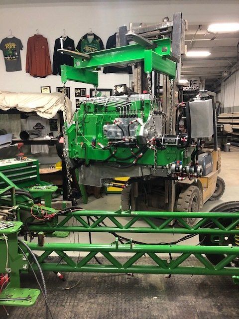 Green agricultural sprayer being worked on inside a shop, mounted on a forklift.