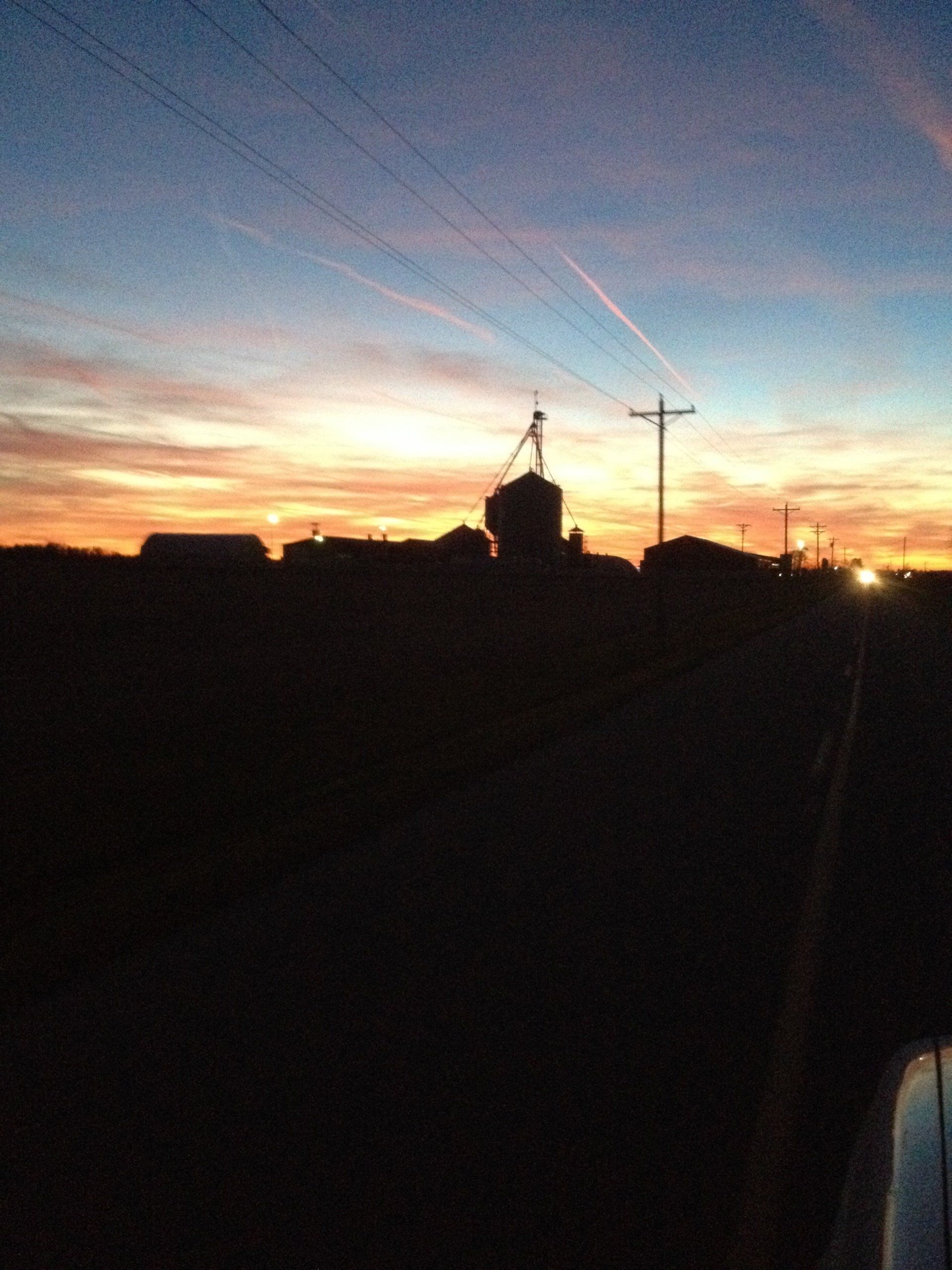 Silhouette of buildings and power lines against a colorful sunset sky.
