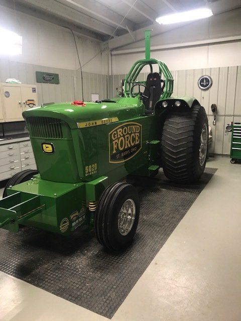 Green John Deere pulling tractor in a garage with large rear tires, a roll cage, and 