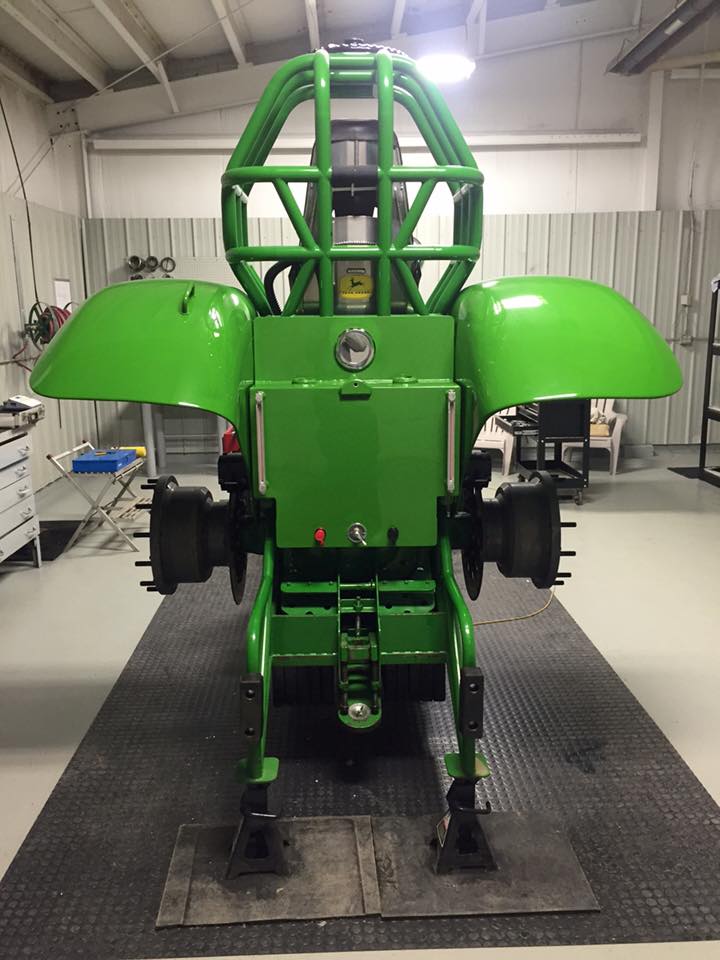Green mechanical robot frame with large wheels and protective cage in a workshop.