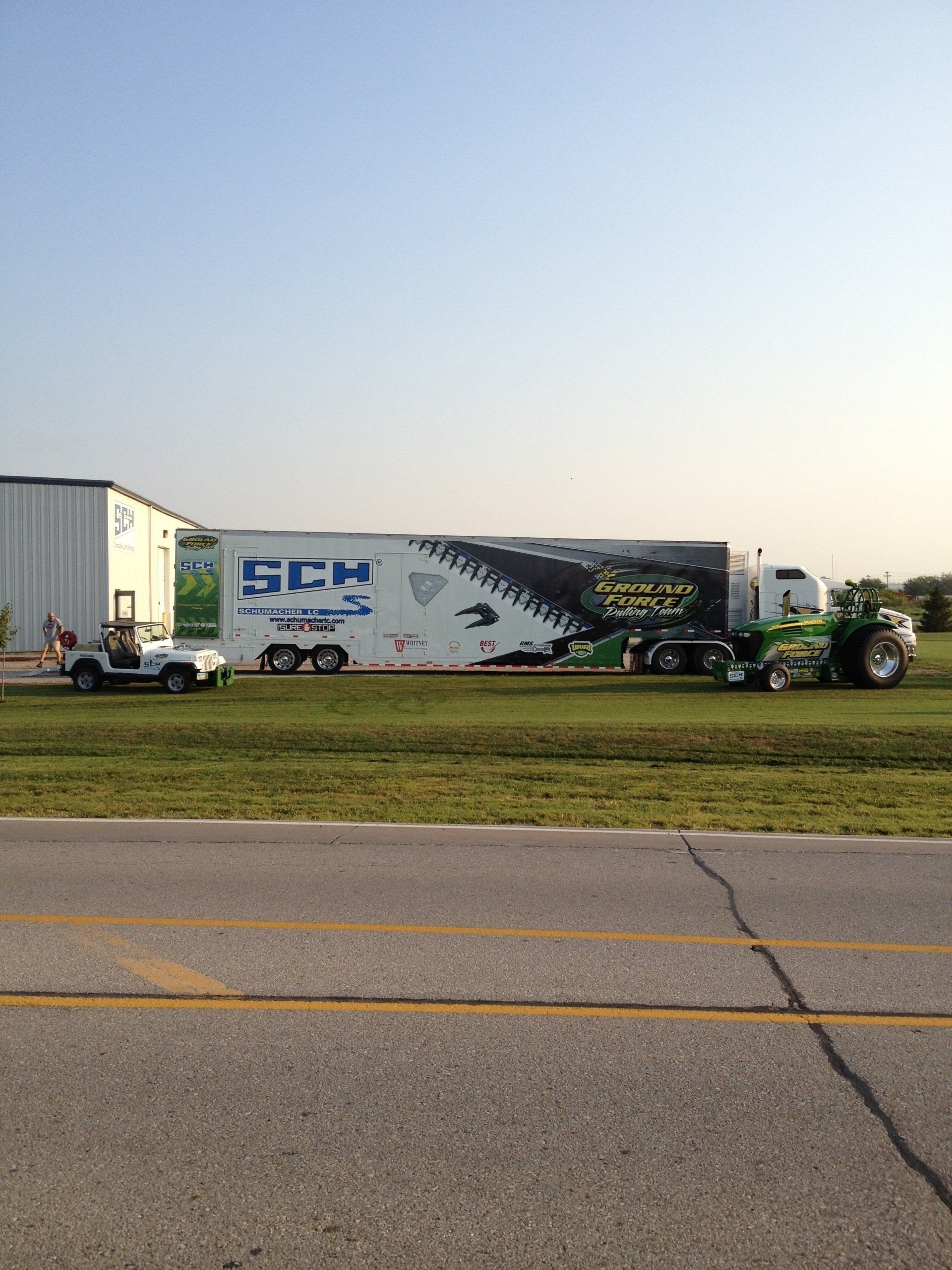 Truck with trailer and tractor on grass by building.
