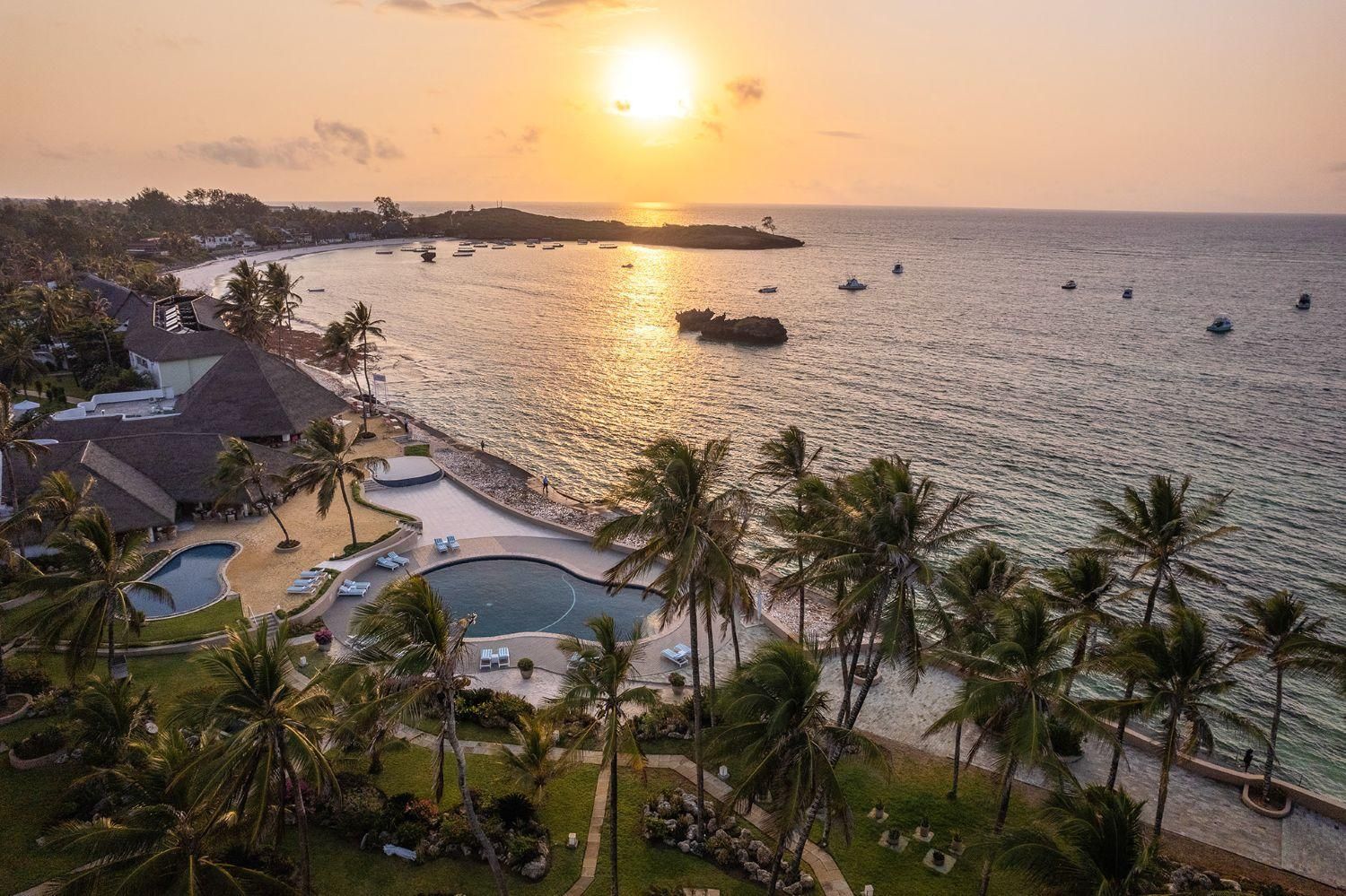 An aerial view of a swimming pool surrounded by palm trees and chairs at sunset.