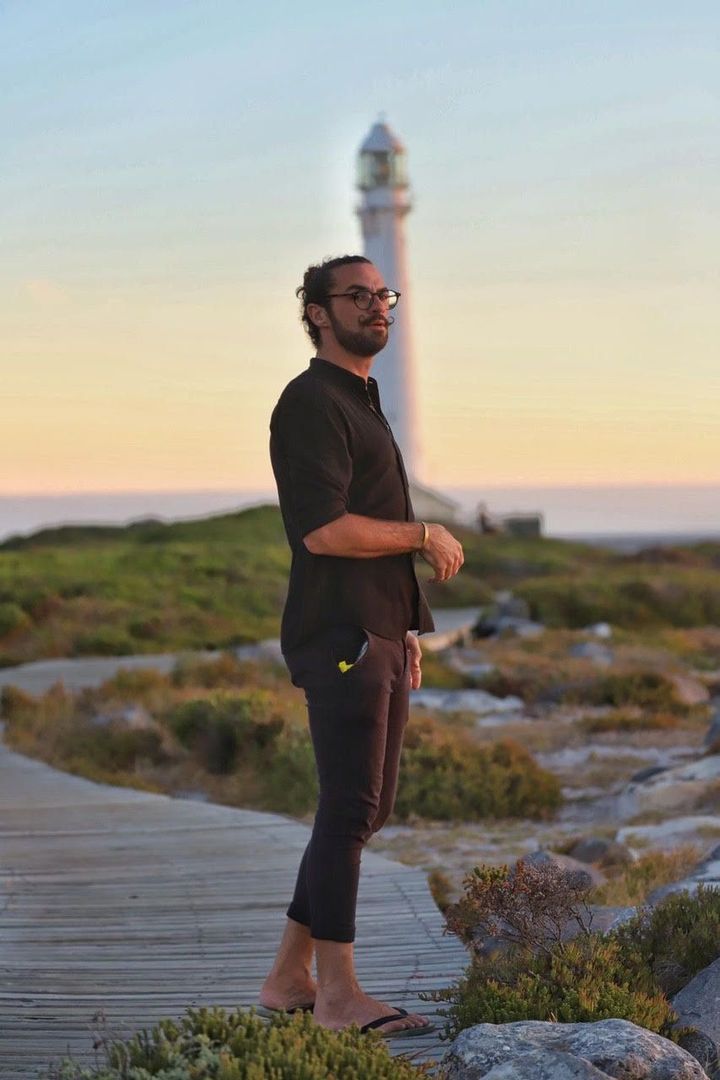 A man is standing on a wooden walkway in front of a lighthouse.
