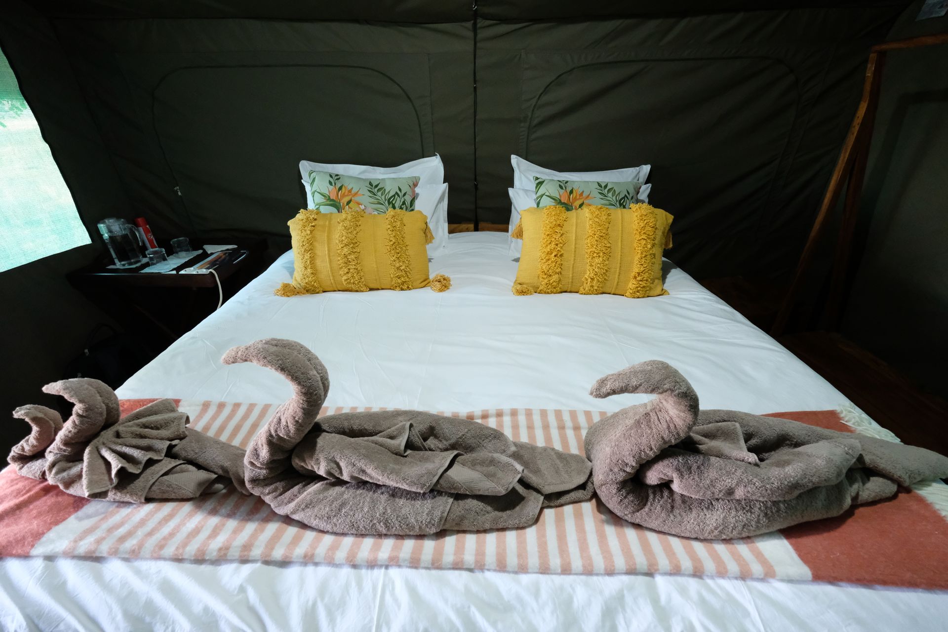 A bed with two pillows and towels on it in a tent.
