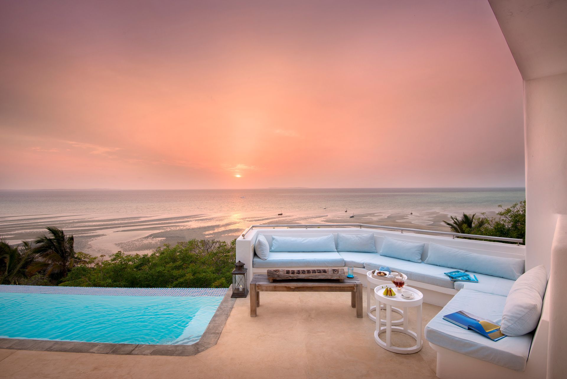 A patio with a swimming pool and a view of the ocean at sunset.