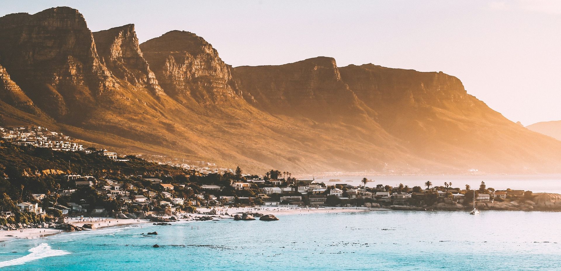 A beach with mountains in the background and a body of water in the foreground.