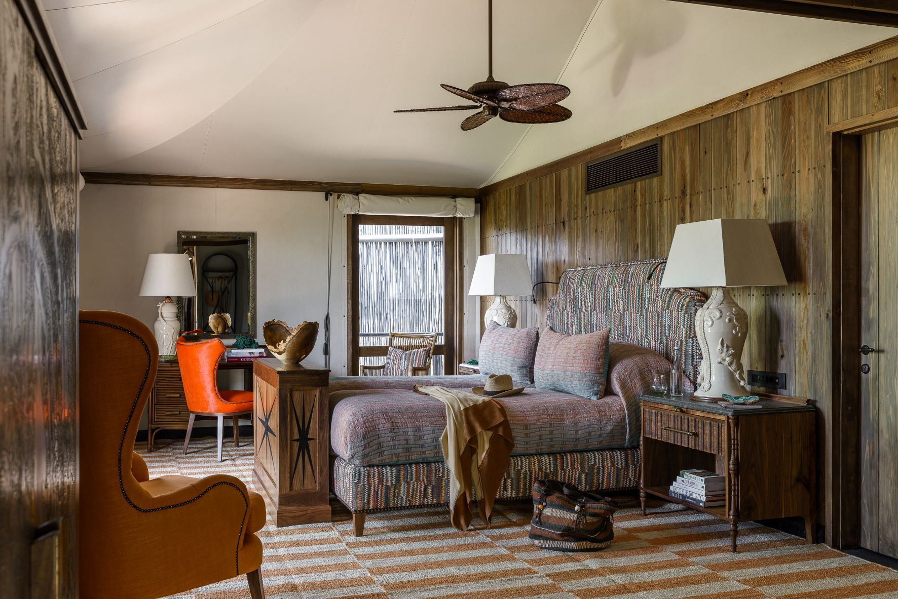 A bedroom with a bed , chairs , lamps and a ceiling fan.