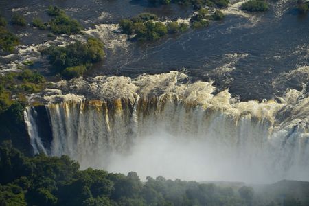 Aerial view of the massive Victoria Falls, featuring rushing water plummeting over a cliff into a misty gorge.