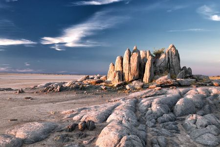 Jagged rock formations rise from a desert landscape under a deep blue sky with streaky clouds.