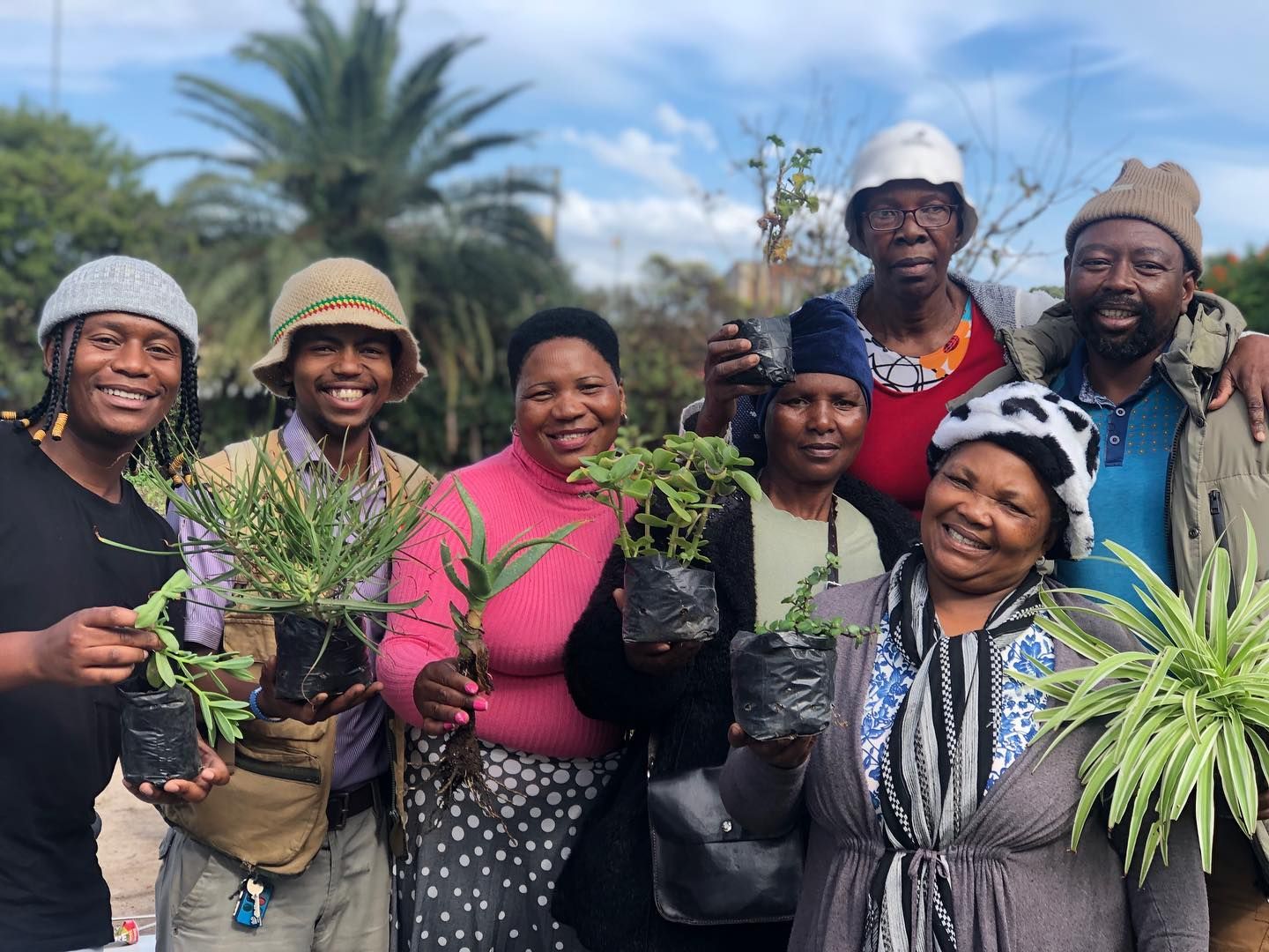 A group of people are posing for a picture while holding potted plants.