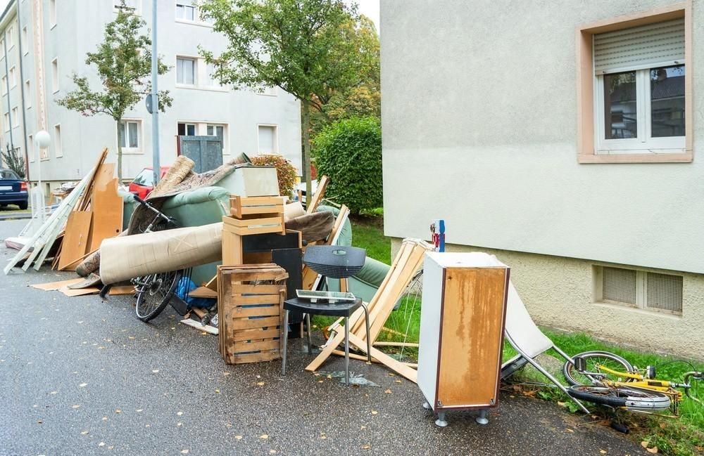 Pile of discarded furniture and debris on a wet street in front of a building.