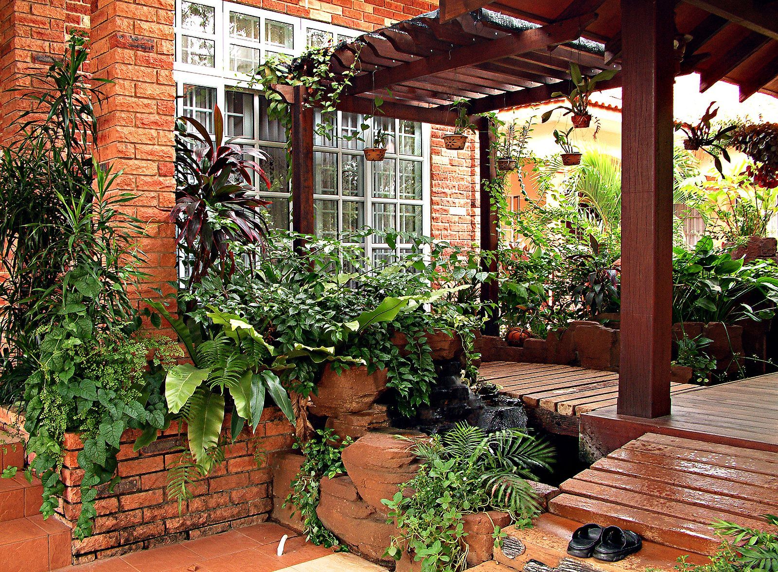 A brick house with a wooden pergola and lots of plants
