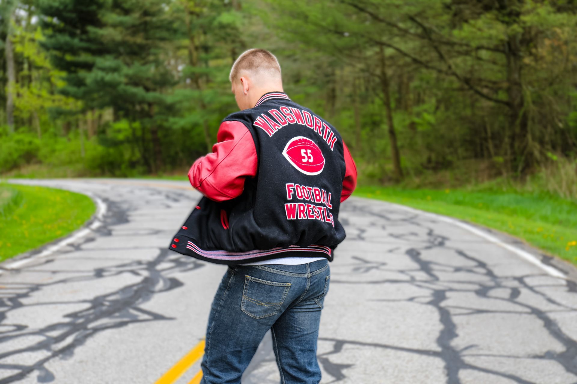 A man wearing a varsity jacket is standing on a road.