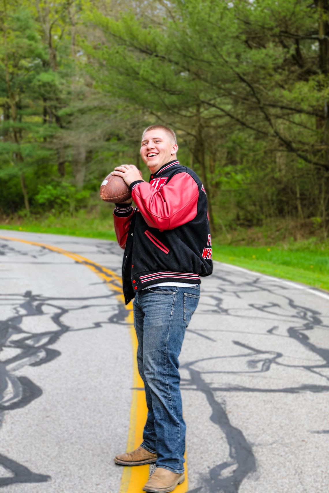 A young man is standing on the side of a road holding a football.