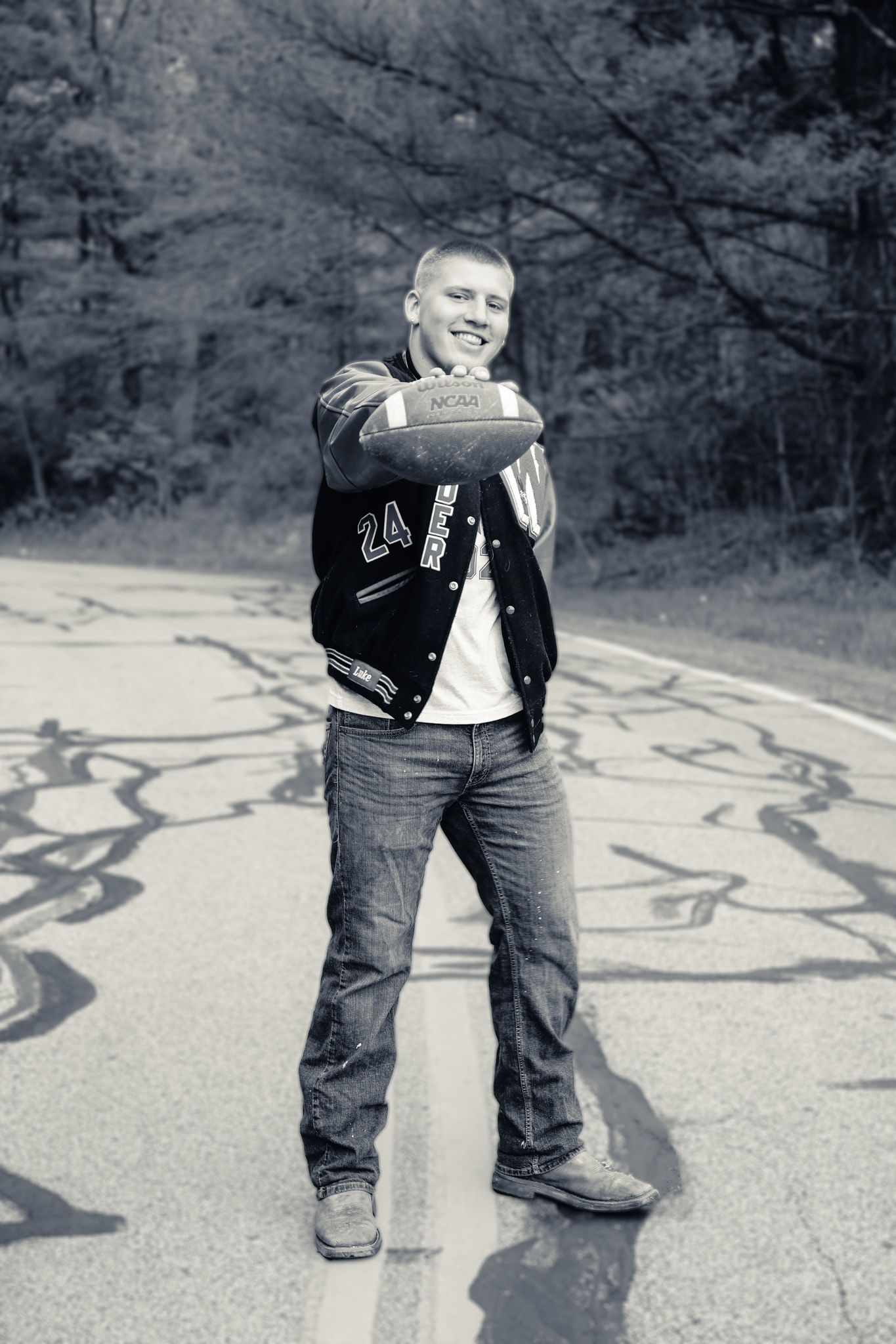 A man in a varsity jacket is standing on the side of a road.