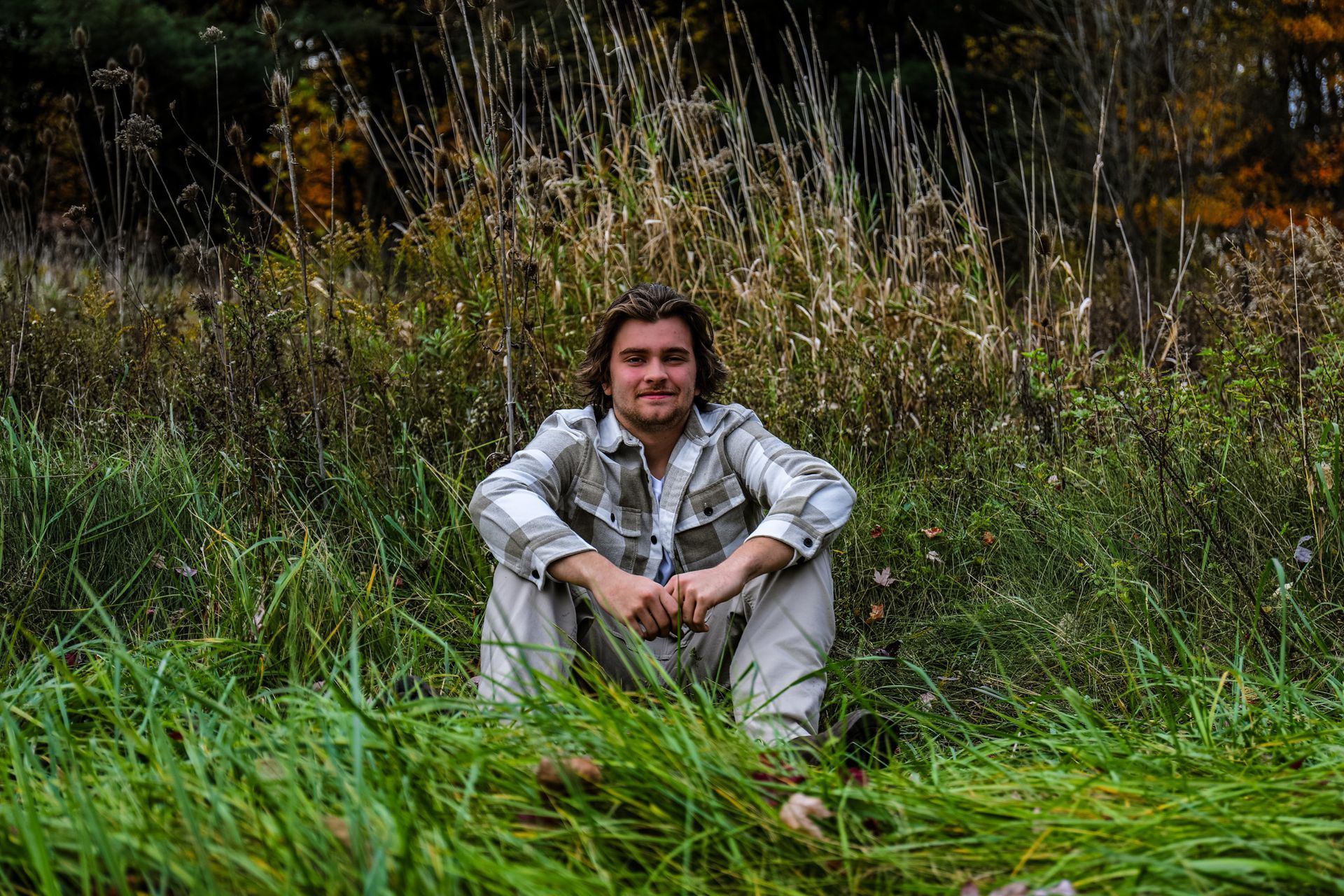 A young man is sitting in the grass in a field.