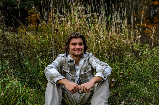 A young man is sitting in the grass in a field.