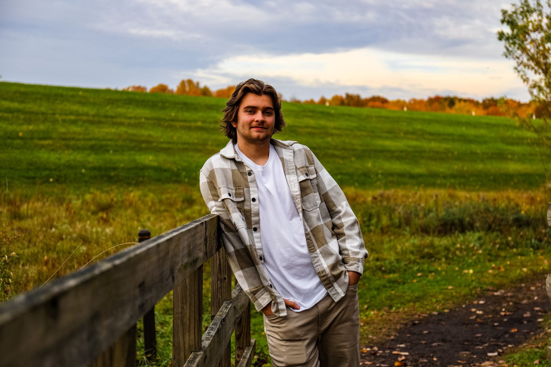 A young man is leaning against a wooden fence in a field.