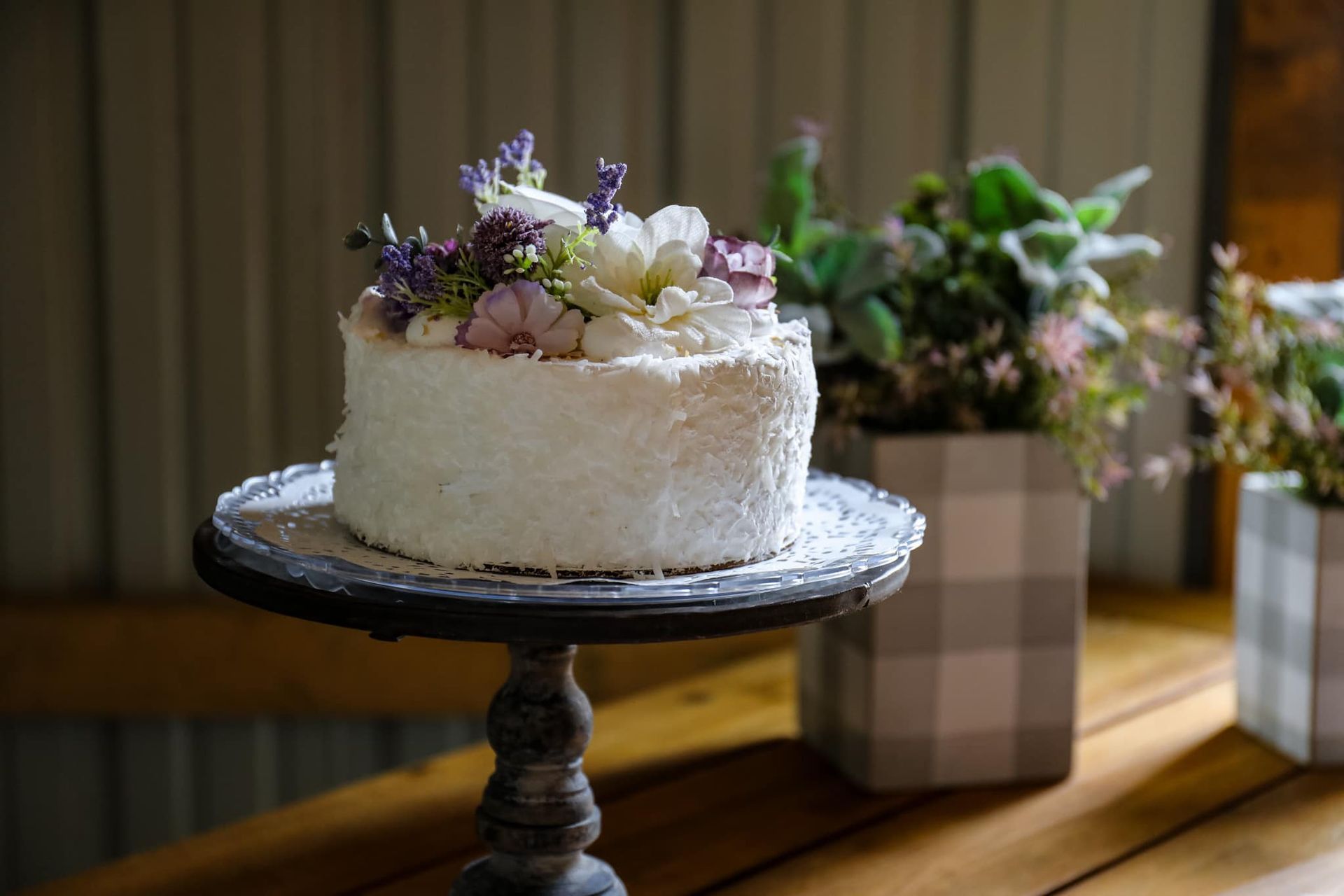 A cake with flowers on top of it is on a cake stand on a table.