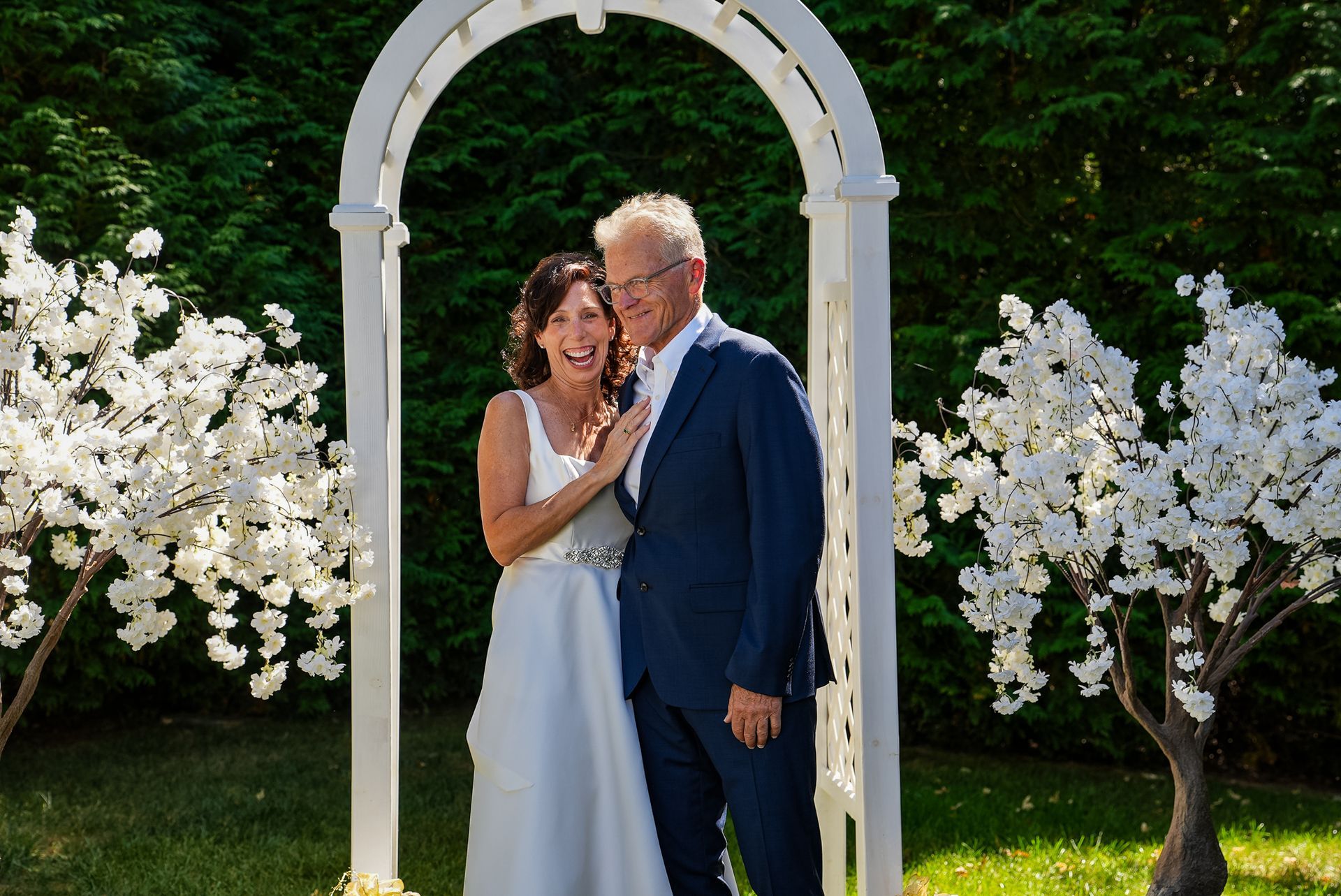 A bride and groom are posing for a picture under a white arch.