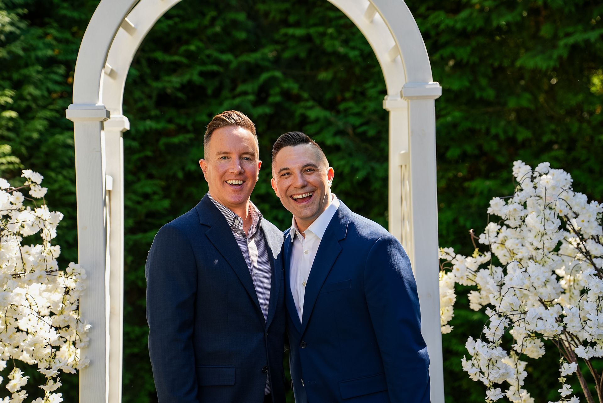 Two men in suits are posing for a picture in front of a white archway.