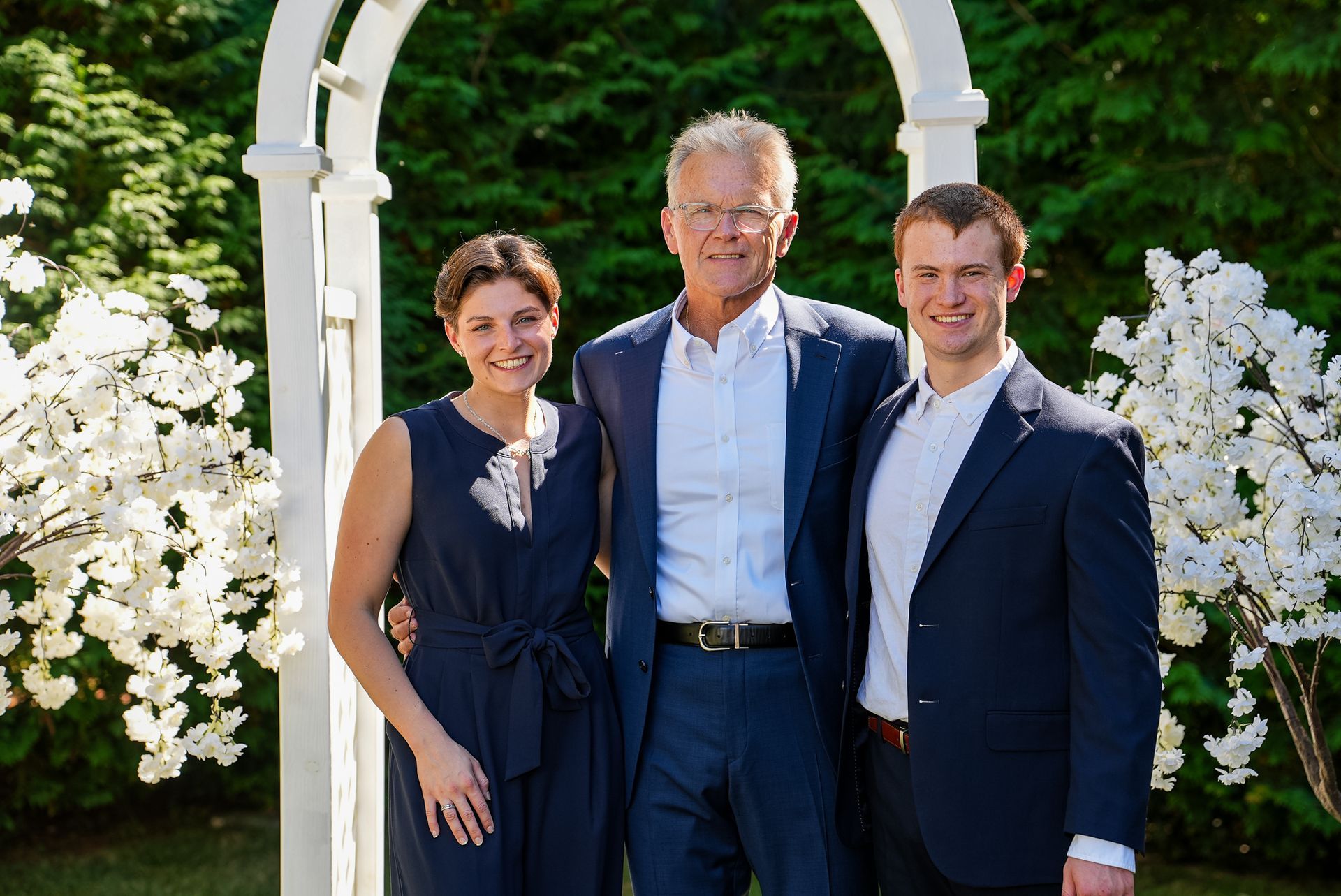 A man and two men are posing for a picture in front of a white arch.