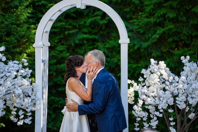 A bride and groom are kissing under an arch at their wedding ceremony.