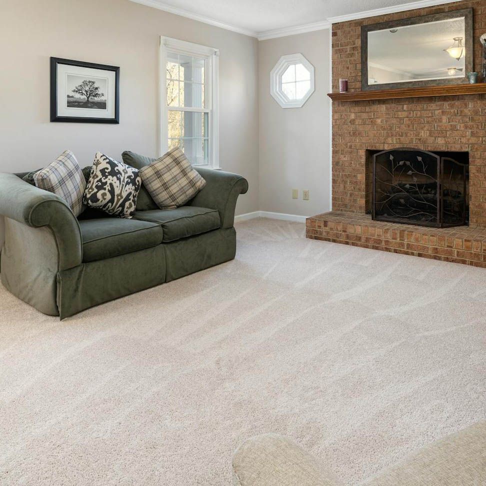 A living room with a green sofa, brick fireplace, and light beige carpet.