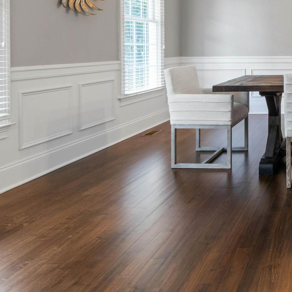 Hardwood floor in a dining room with white wainscoting and a dark wood table and chair.