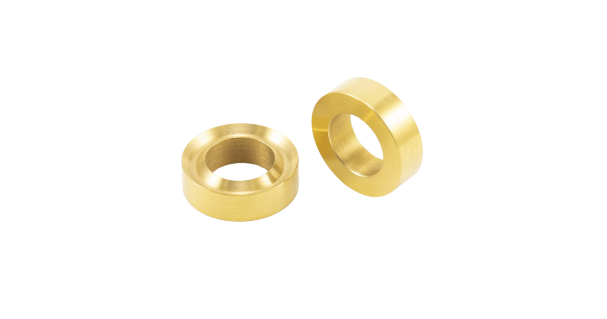 Two gold-colored brass bushings with a centered hole, lying on a white background.
