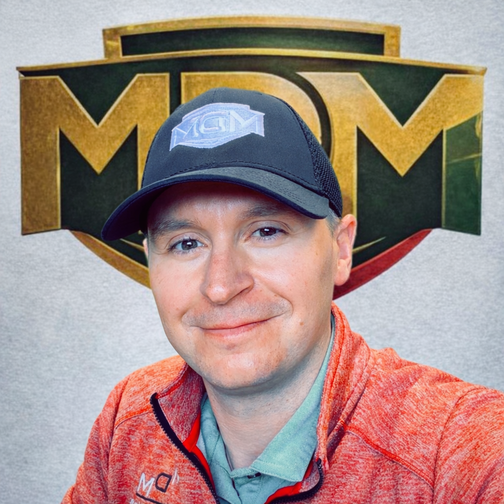 Man in blue zip-up smiling, in an industrial setting.