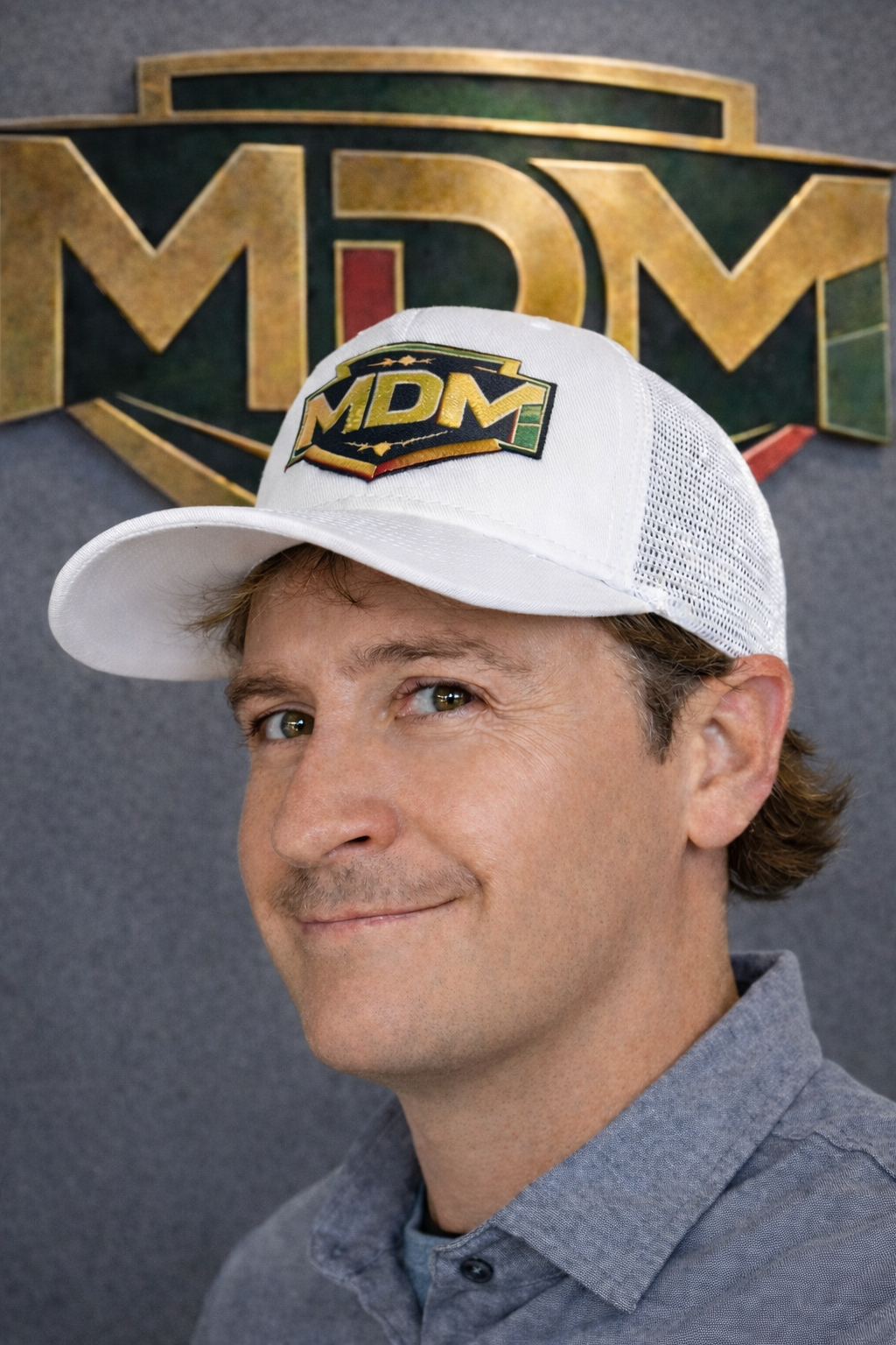 Man in blue zip-up smiling, in an industrial setting.