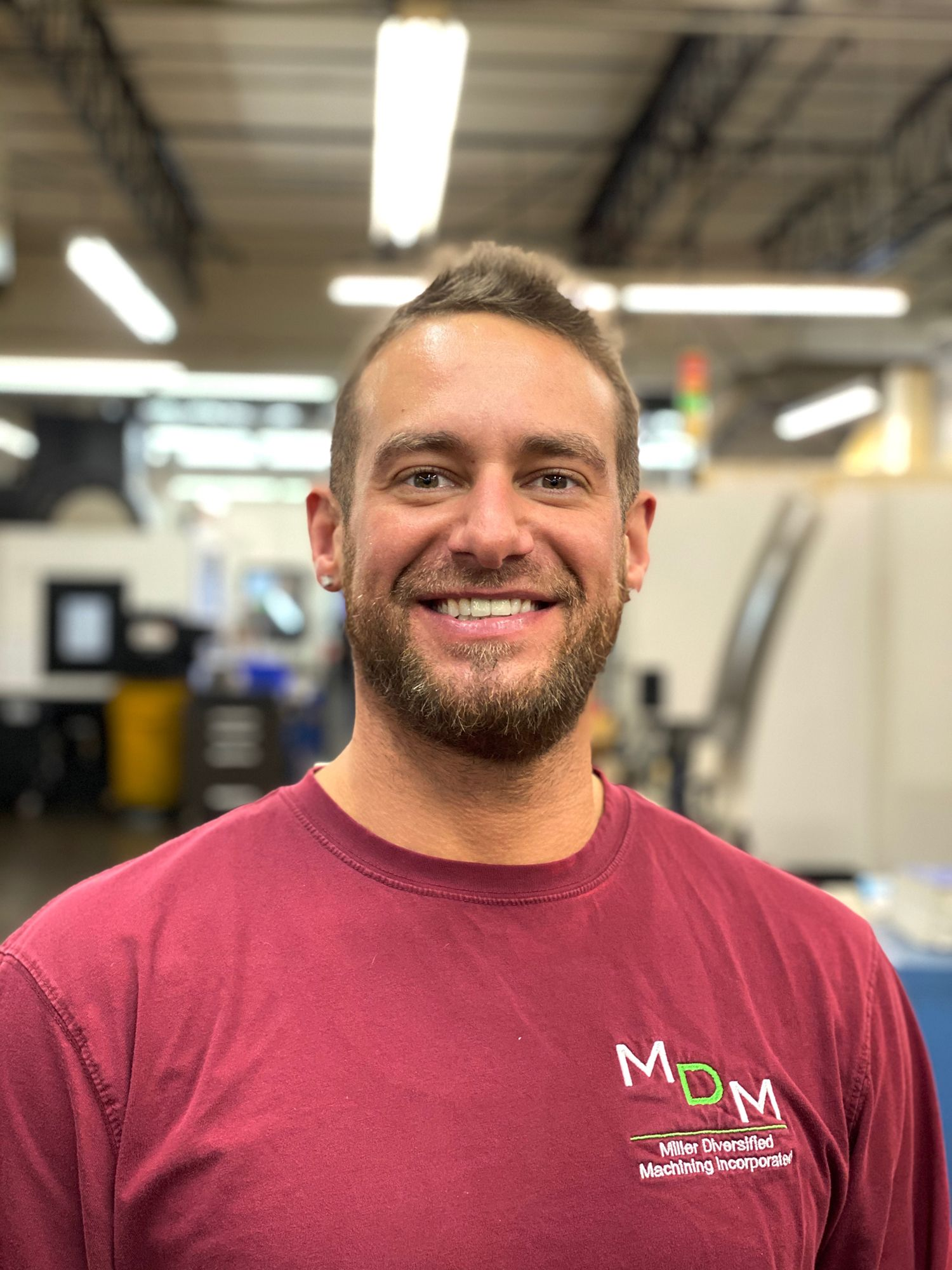 Man in maroon shirt smiling in a machine shop.