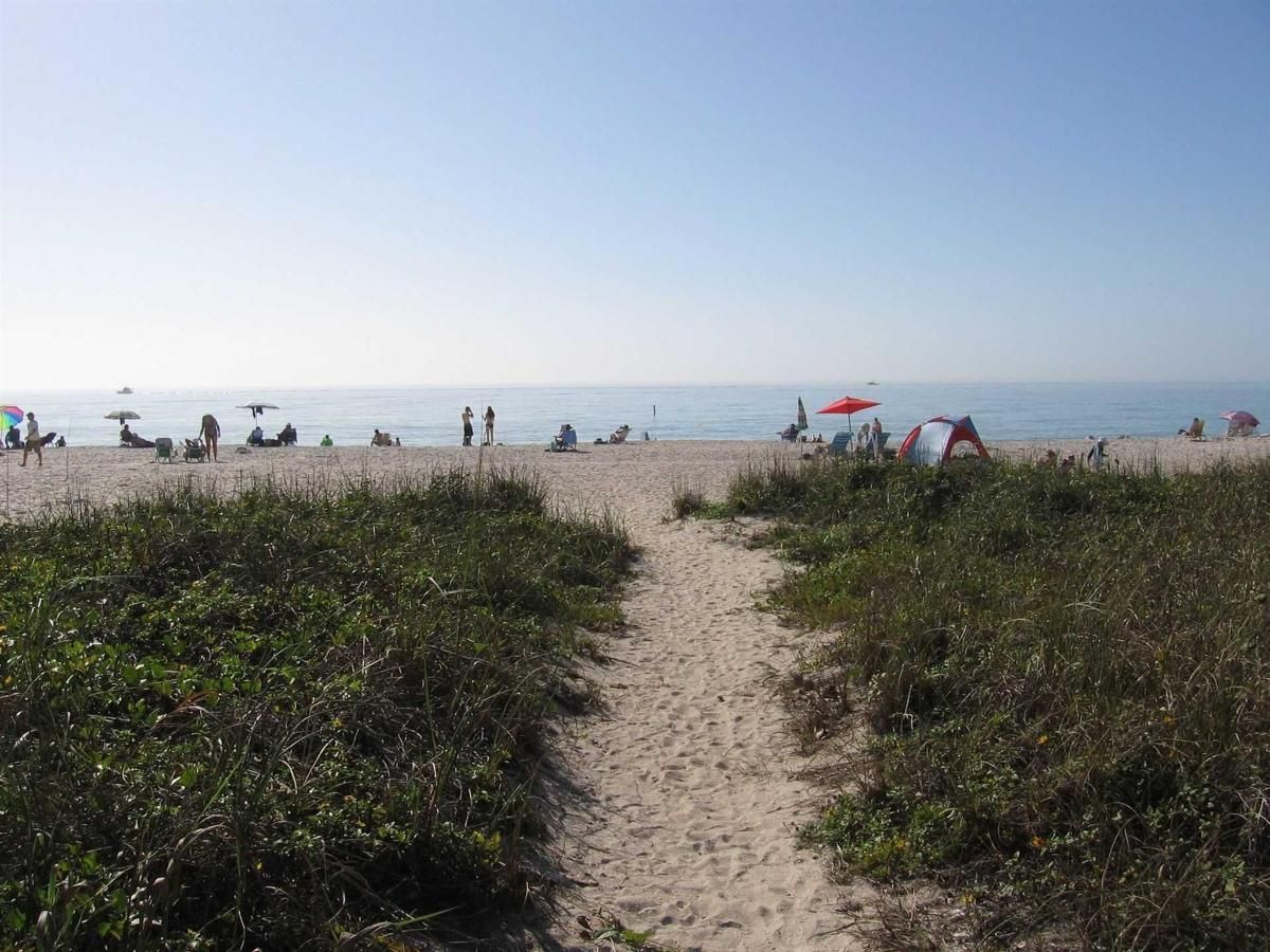 A path leading to a beach with people sitting under umbrellas