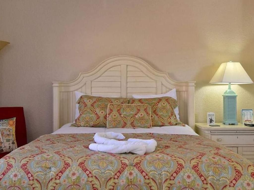 A hotel room with a bed, nightstand, lamp and chair.