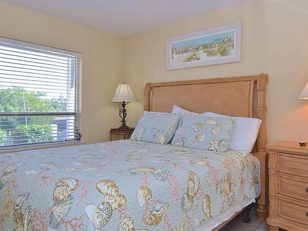 A bedroom with a bed , nightstand , lamp and window.