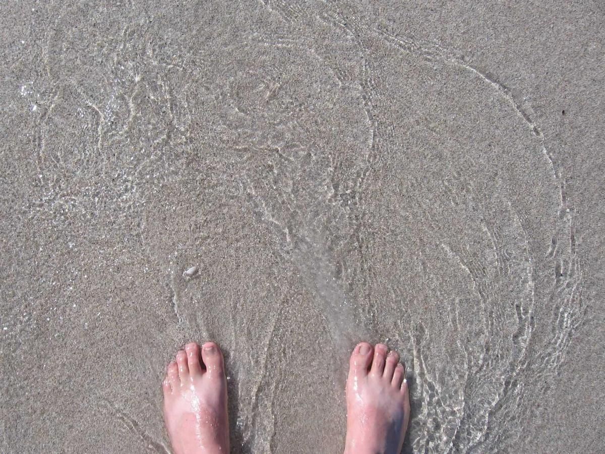A person 's feet are standing in the sand on a beach.