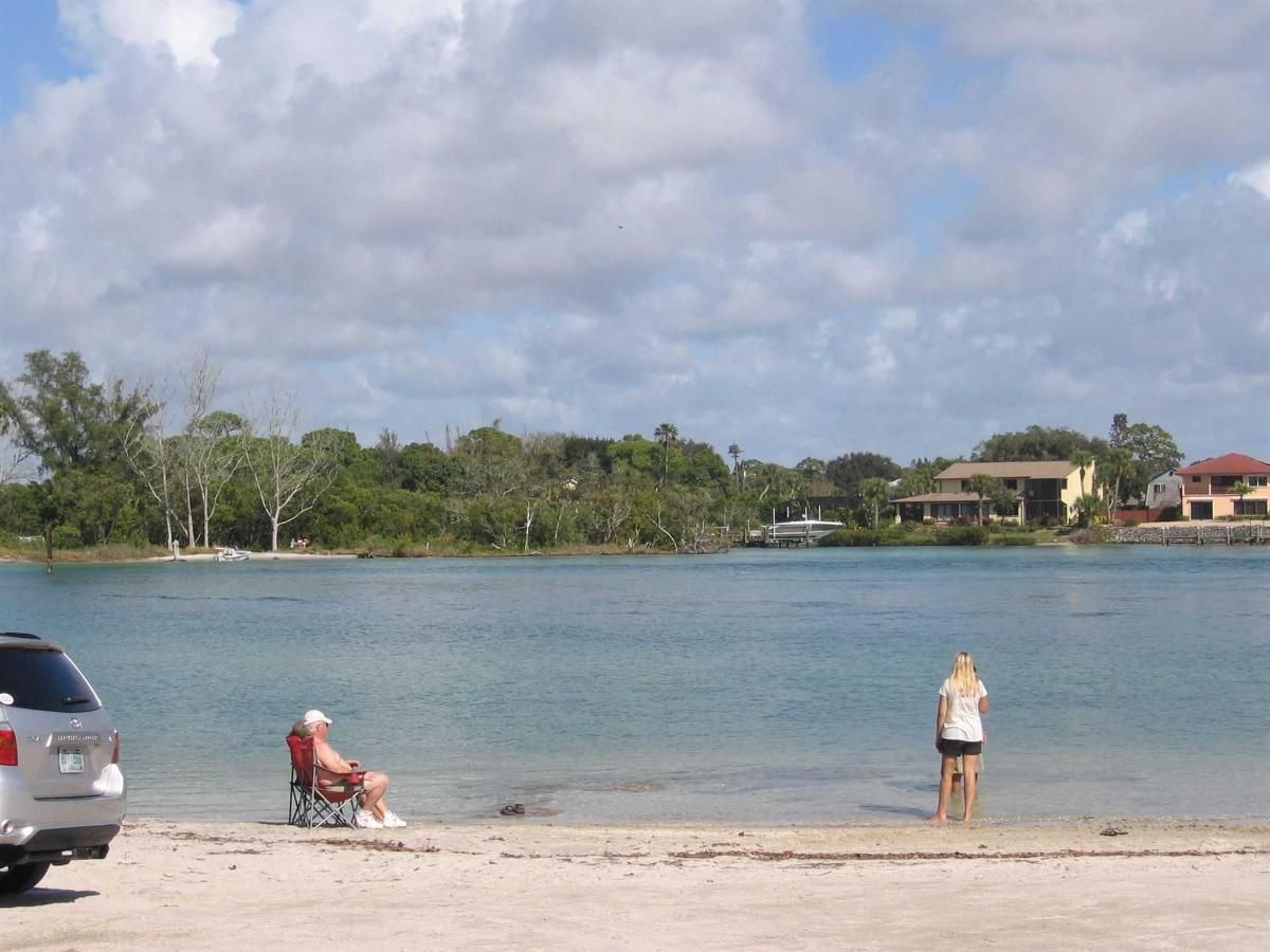 A man sits in a chair on the beach while a woman stands in the water.