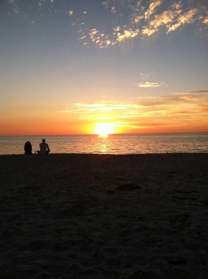 Two people are sitting on the beach watching the sun set over the ocean.