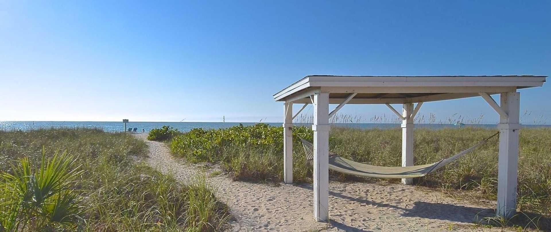There is a hammock under a gazebo on the beach.