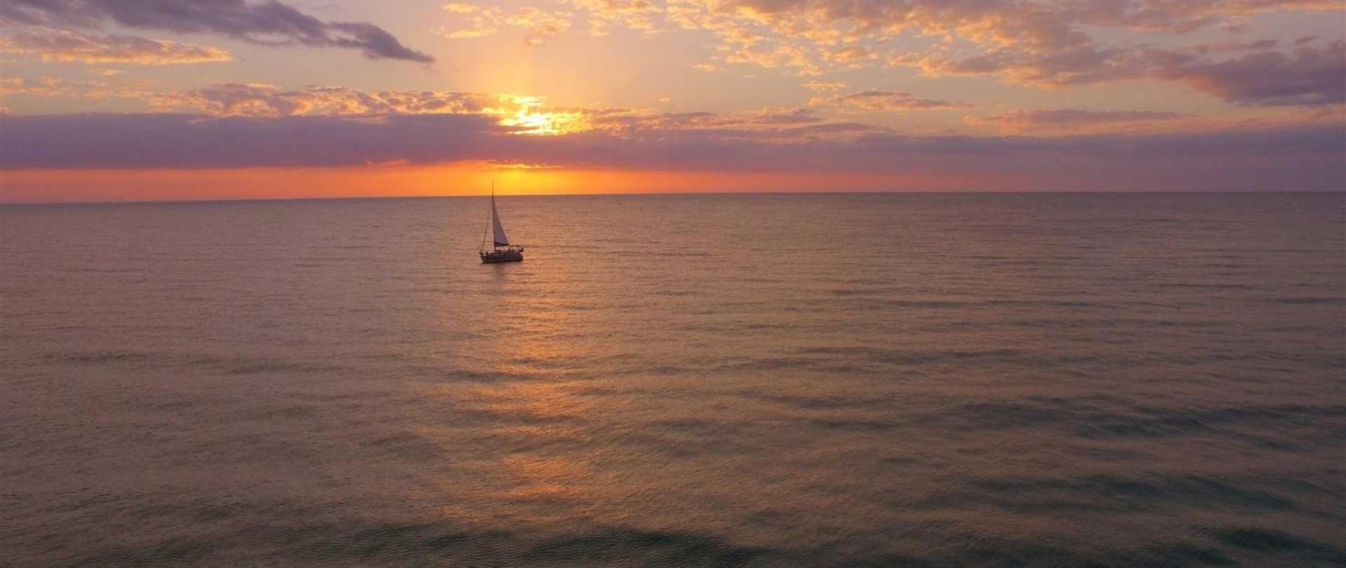 A boat is floating on top of a body of water at sunset.